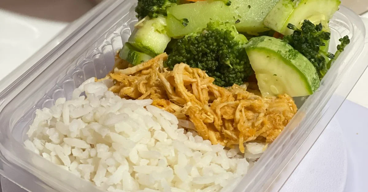Une boîte repas nutritive avec du riz, du poulet effiloché et des légumes mélangés.