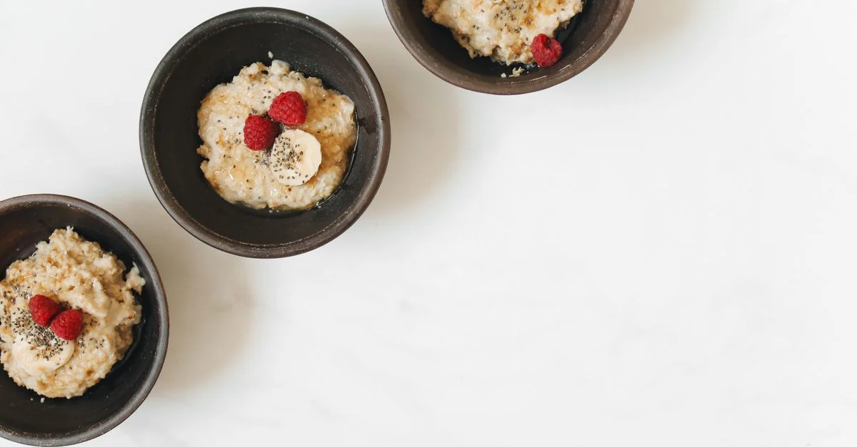 Bol de flocons d'avoine avec banane, framboise et graines de chia sur un fond blanc.
