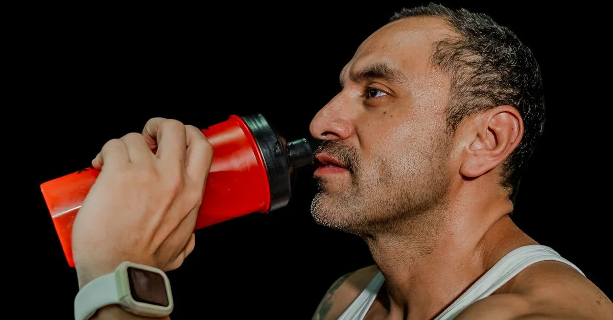 Homme adulte en forme buvant d'une bouteille de shaker, axé sur la fitness, arrière-plan noir.