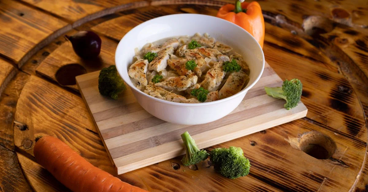 Une soupe au poulet copieuse avec des légumes, joliment présentée dans un bol blanc sur une table en bois rustique.