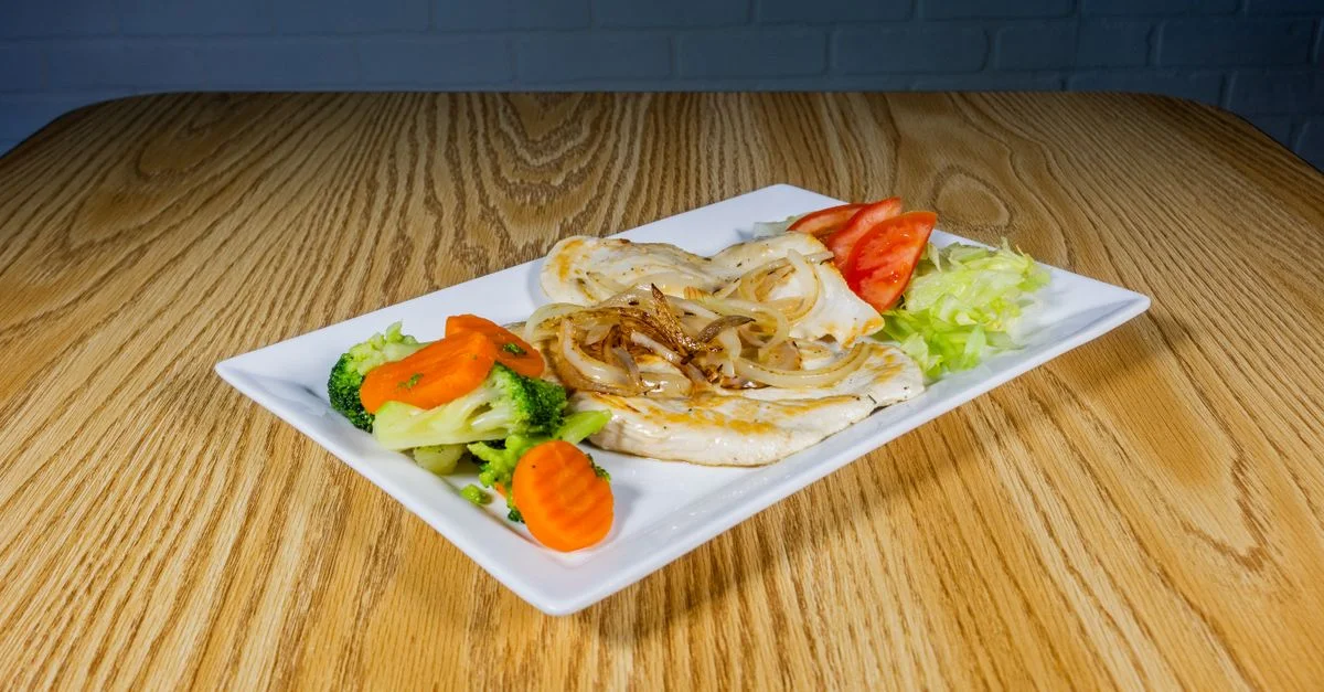 Une assiette de poulet grillé avec des légumes et des oignons sur une table en bois.