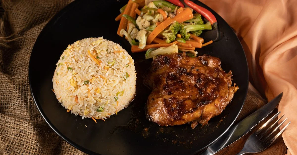 Une délicieuse présentation mettant en avant du poulet grillé, du riz sauté et des légumes sautés sur une assiette noire.