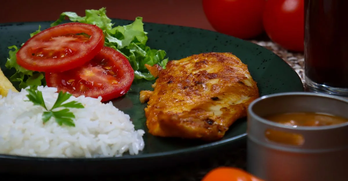 Un repas appétissant composé de poulet grillé, de riz, de tomates fraîches et de salade dans une assiette noire.