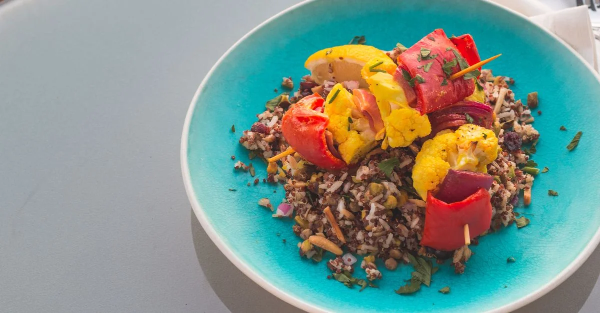 Salade de quinoa colorée garnie de légumes grillés sur une assiette bleue.