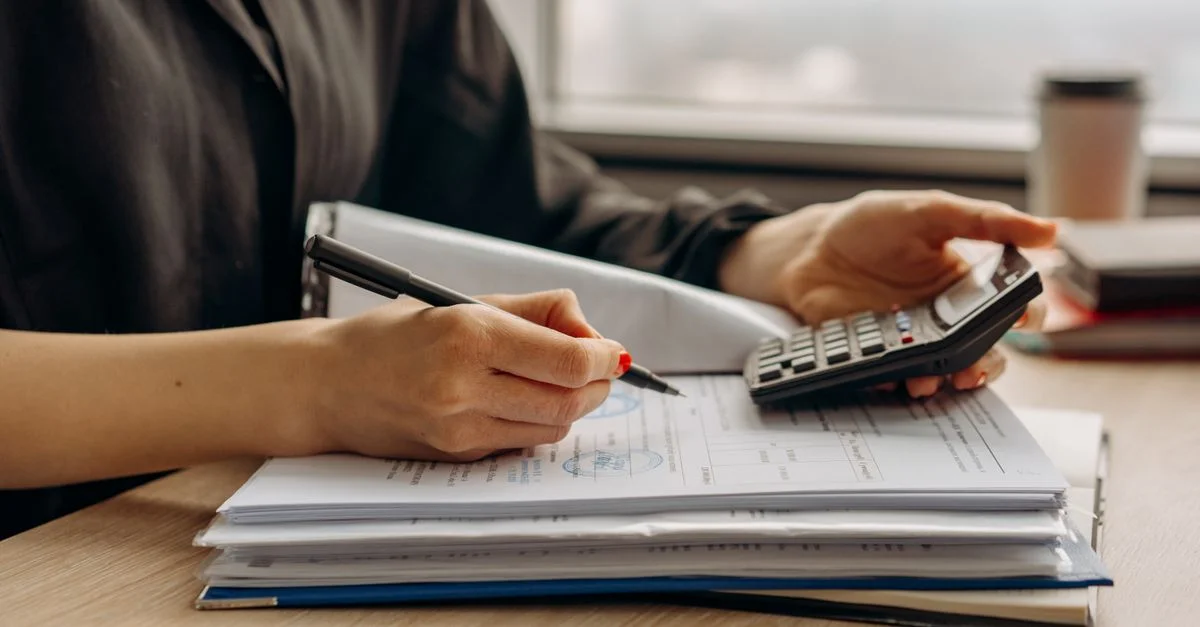 Gros plan d'une personne utilisant une calculatrice avec des documents financiers dans un bureau.